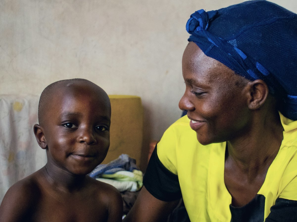 A caregiver in a blue headwrap smiling at a young child