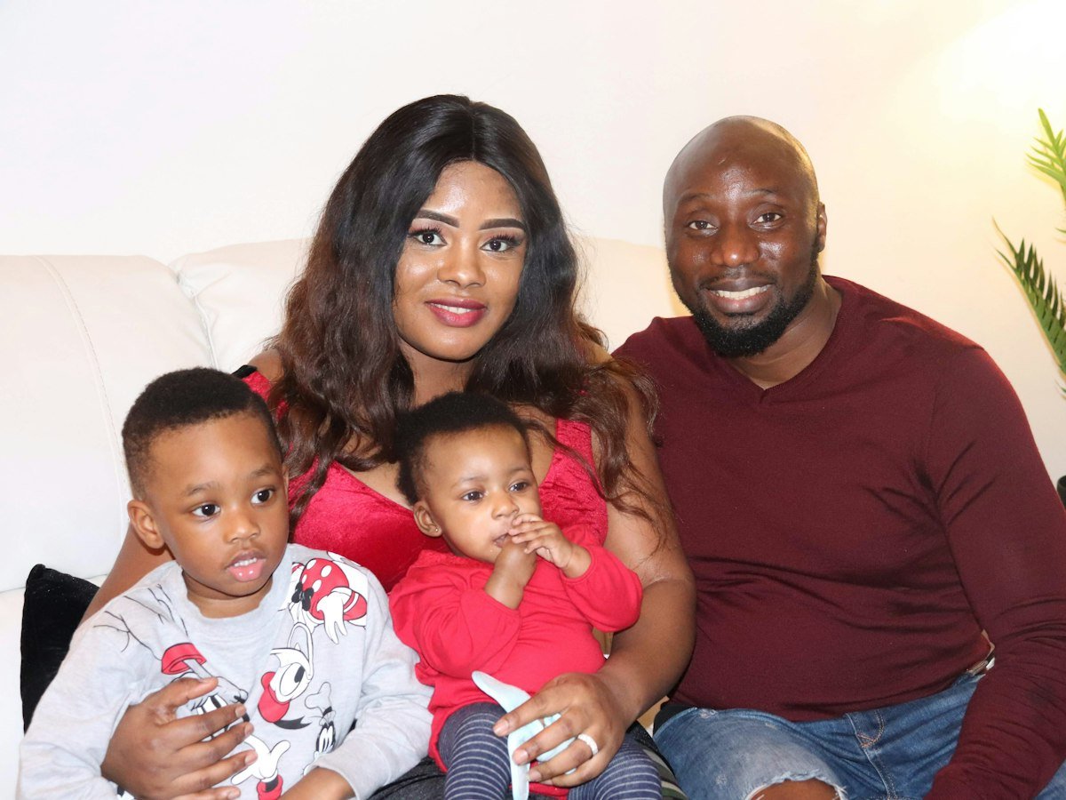 A smiling mother and father sitting on a sofa with their two young children
