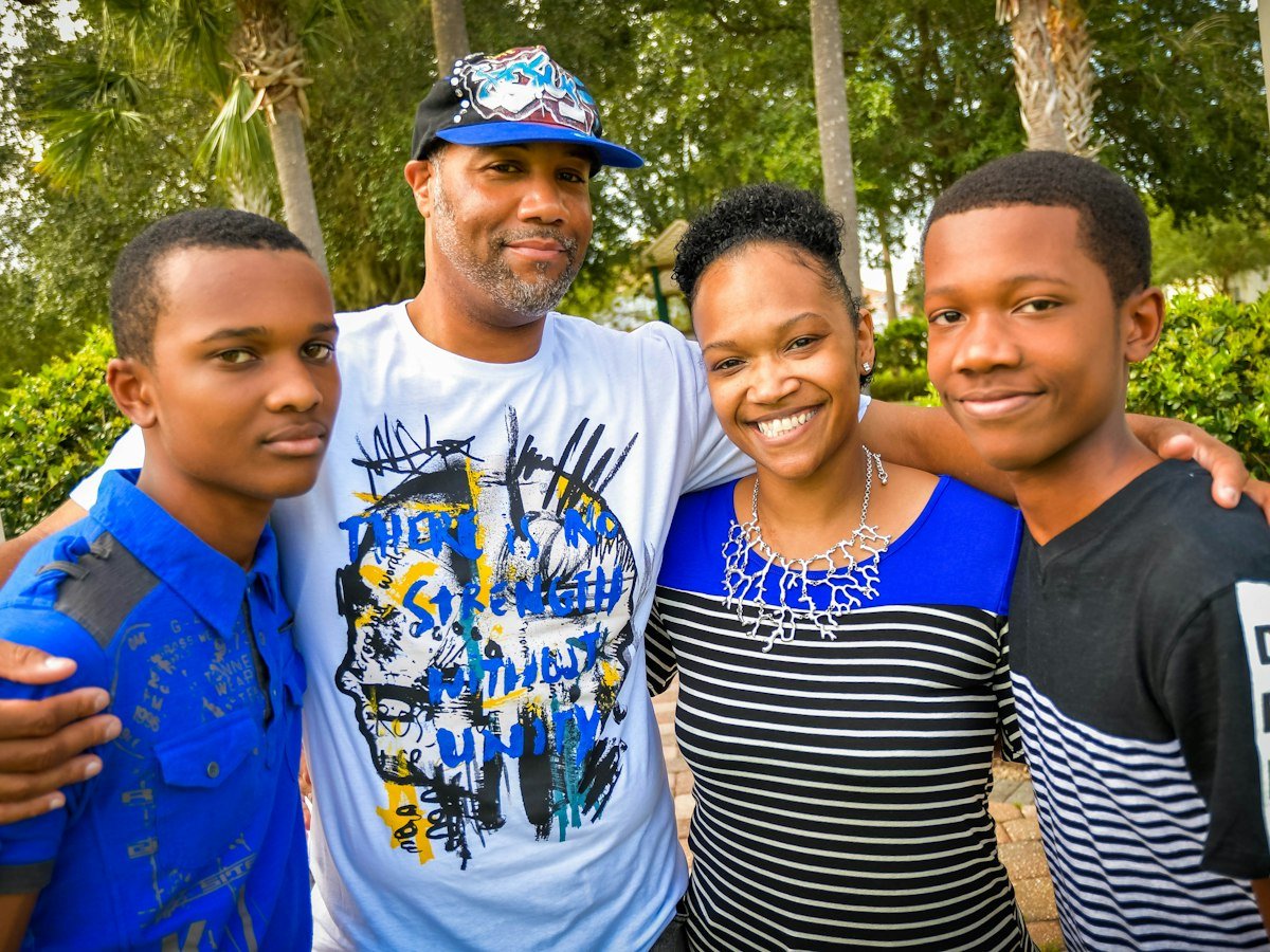 A father and mother with their arms around their two teenage sons outdoors